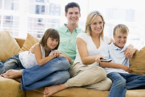 Families Sitting In Living Room With Remote Control Smiling